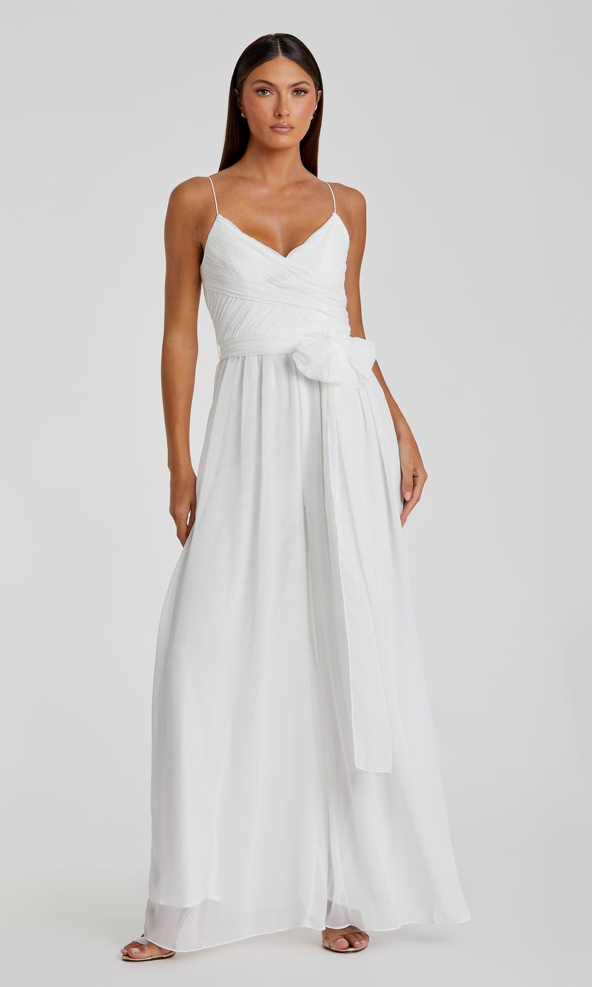 A woman models the Flowing Wide-Leg Formal Jumpsuit: Mac Duggal 70100, featuring a V-neckline, spaghetti straps, and a wide sash at the waist—the ideal long jumpsuit for prom—against a plain background.